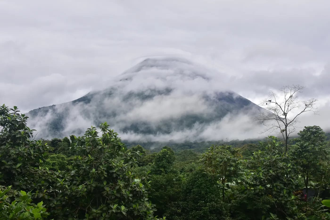 Clouds around Arenal Volcano above green forest